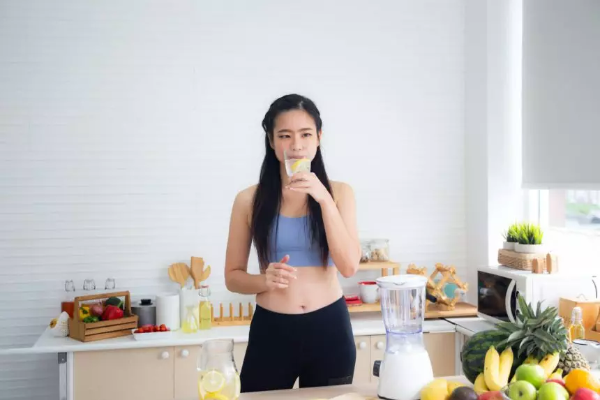 Fit and healthy young Asian woman in sportswear preparing and drinking fresh lemon water