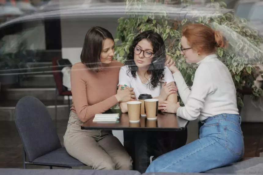 three women comfort each other and help in difficult times. friends talk in a coffee shop and drink