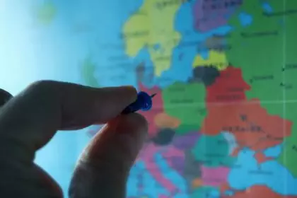 World map and in front of the map close up hand holding pushpin. Choose the destination.