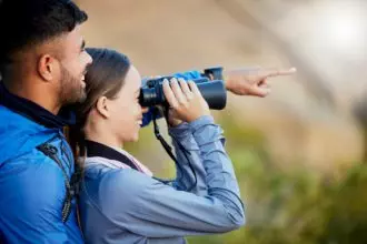 Binoculars, pointing and a couple bird watching in nature while hiking in the mountains together. F