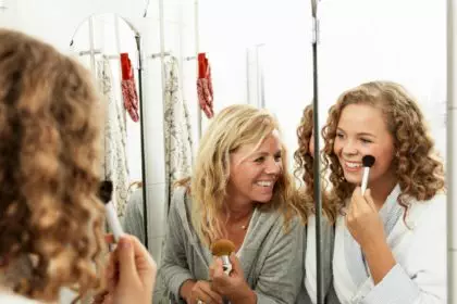 Mature woman applying make-up with daughter in mirror