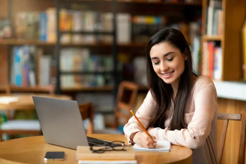 Online education. Motivated latin female studying with laptop at cafe and taking notes while