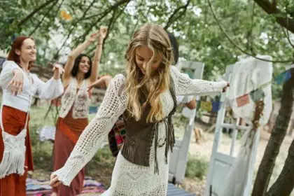 young blonde woman in boho styled dress dancing near blurred multiethnic friends in retreat center