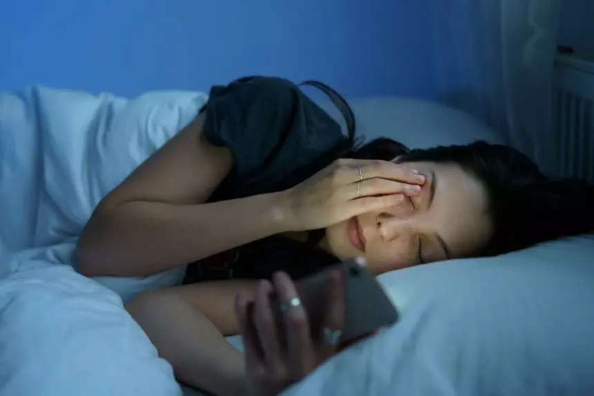 Exhausted woman looking at smartphone screen, lying in bed late at night. Social media addiction