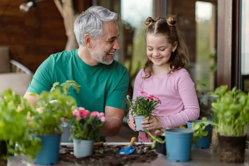 Little daughter helping father to plant flowers, home gardening concept