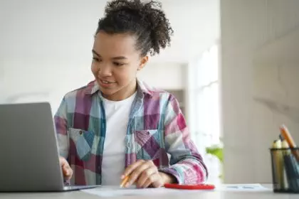 Mixed race student teenage school girl learns online at laptop. Distance education, e-learning