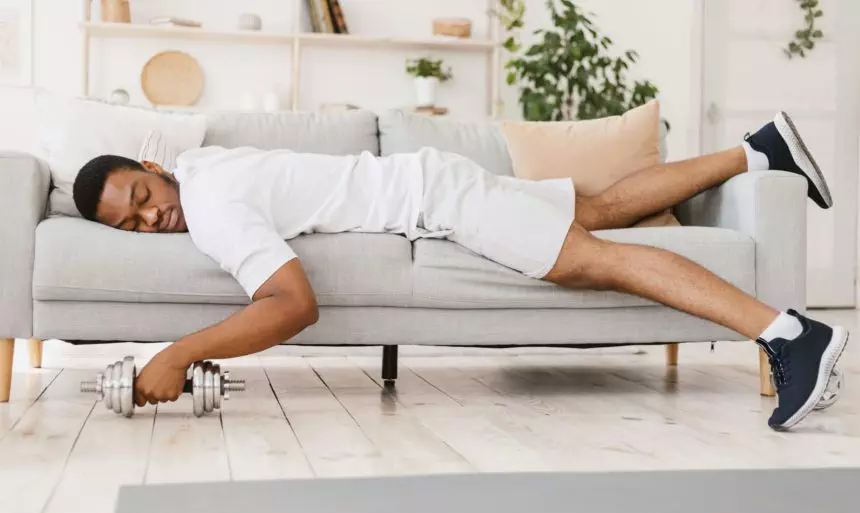 Exhausted Black Man Holding Dumbbell Sleeping On Sofa At Home