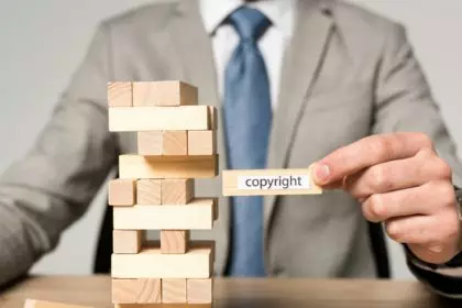 partial view of businessman holding wooden block with copyright inscription isolated on grey