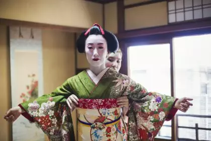 A geisha being dressed in the traditional kimono