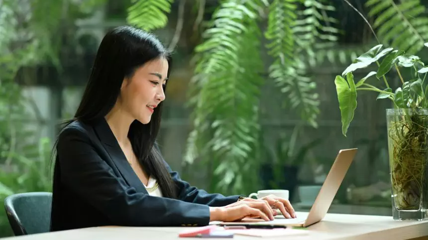 Smiling millennial businesswoman using laptop computer in green eco friendly working space.
