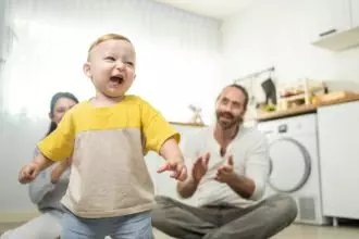 Caucasian baby boy child learn to walk with parents support to develop skill in living room at home.