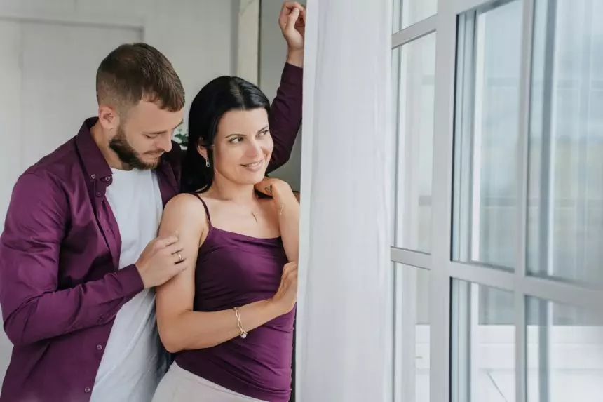 Intimate moment of a couple, man embracing woman near a bright window, both in harmonious purple