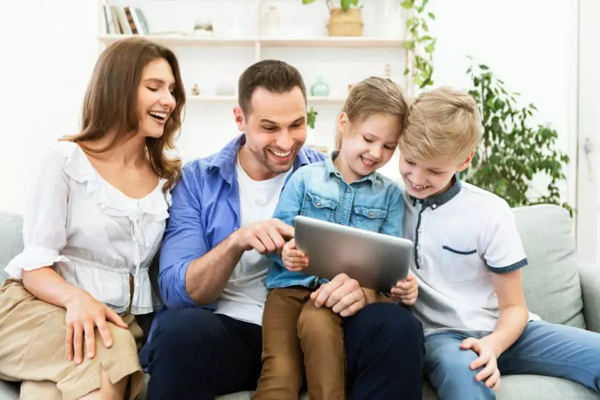 Parents And Children Sitting With Tablet Laughing Sitting At Home