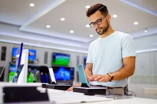 Happy young man trying out new smart phone, digital devices. Tech store interior.